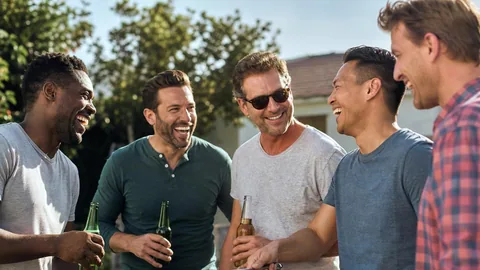 Group of men laughing together around a backyard grill