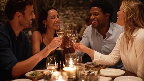 Friends laughing and raising glasses at a candlelit restaurant table